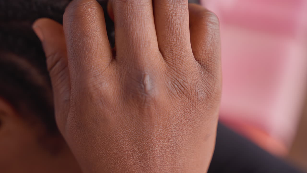 Donna di colore che ispeziona da vicino il cuoio capelluto intrecciato, mano delicata che rivela scaglie secche sulle treccine aderenti, sfondo rosa caldo, ambiente domestico intimo, tocco genitoriale che controlla i bordi e i residui di prodotto.