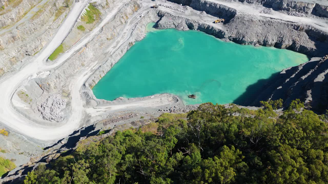 Aerial footage of a quarry with vibrant turquoise water surrounded by rocky terrain and greenery under bright sunlight