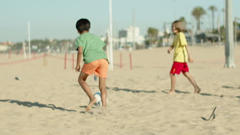 Back-view-of-boy-keeping-goal-and-clearing-ball-on-seashore