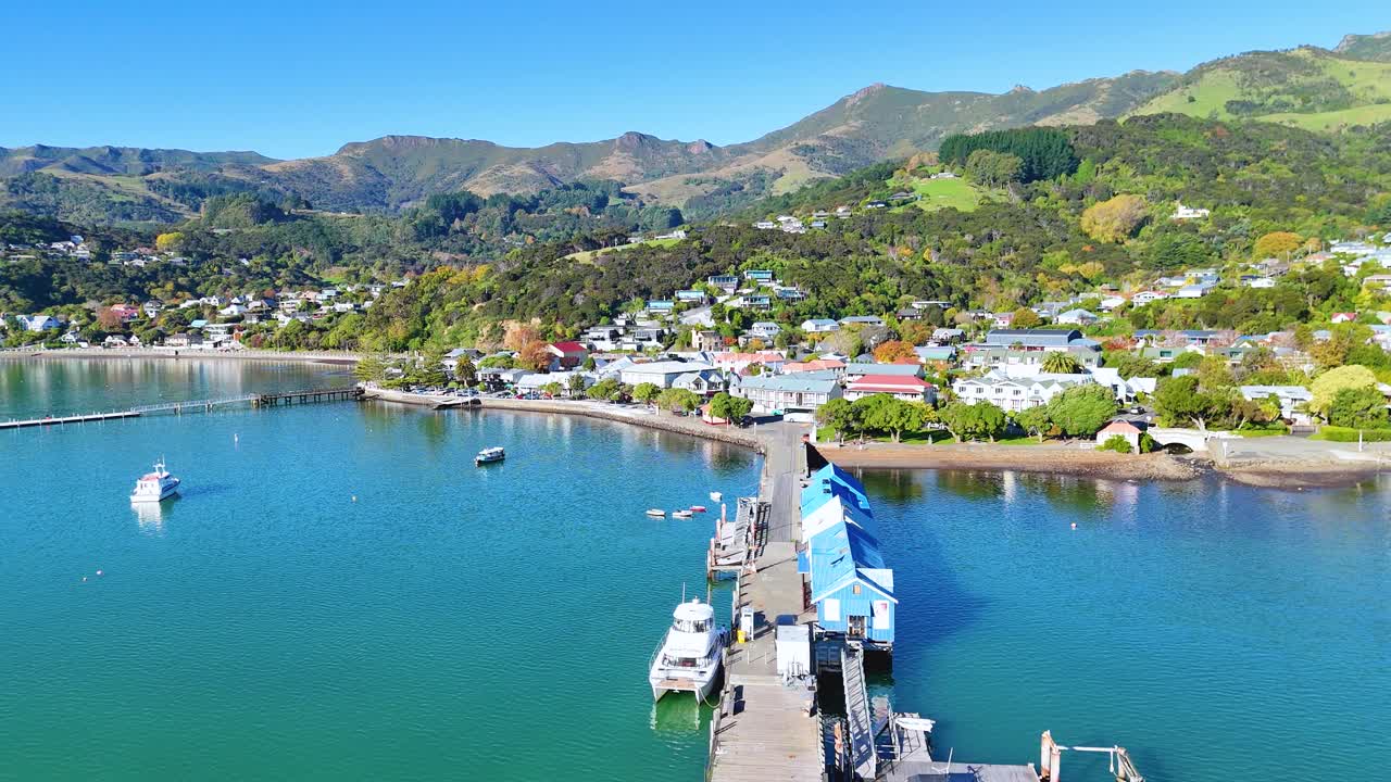 Aerial footage of Akaroa Harbour showcasing boats, piers, and lush hills under clear skies