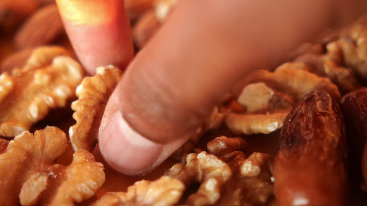 cerca de una mano agarrando una nuez de un cuenco de nueces mezcladas y dátiles
