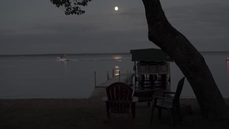 Lake-in-Bemidji,-Minnesota,-during-the-early-evening-with-a-full-moon-with-boats-going-by-in-the-background