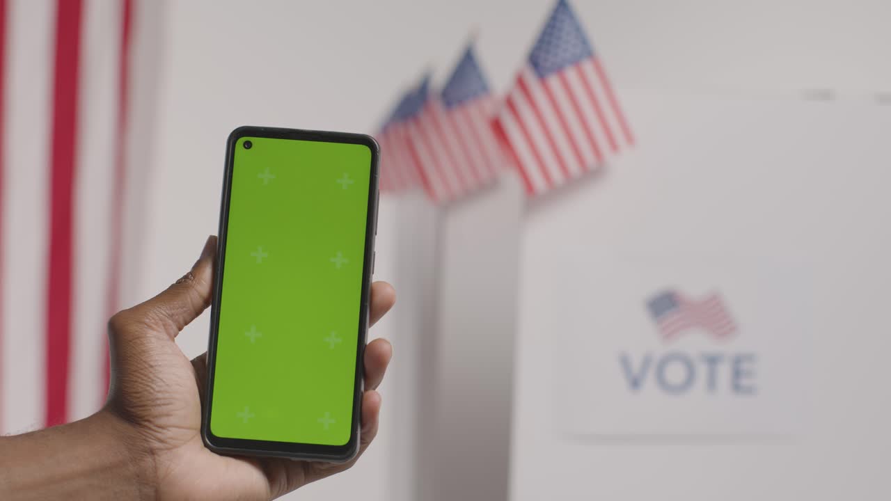 cerca de la mano sosteniendo un teléfono móvil de pantalla verde frente a la urna electoral en las elecciones estadounidenses 1