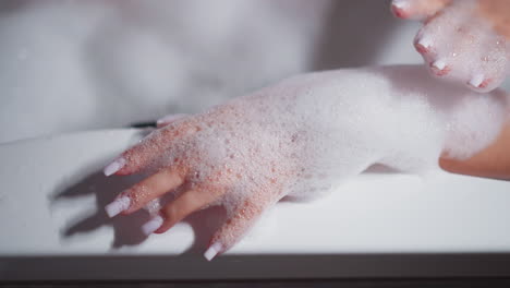 woman applies foam on manicured hand in bathtub closeup. elegant lady takes care of body with cosmetic products in bathtub at home. hygienic routine pleasure