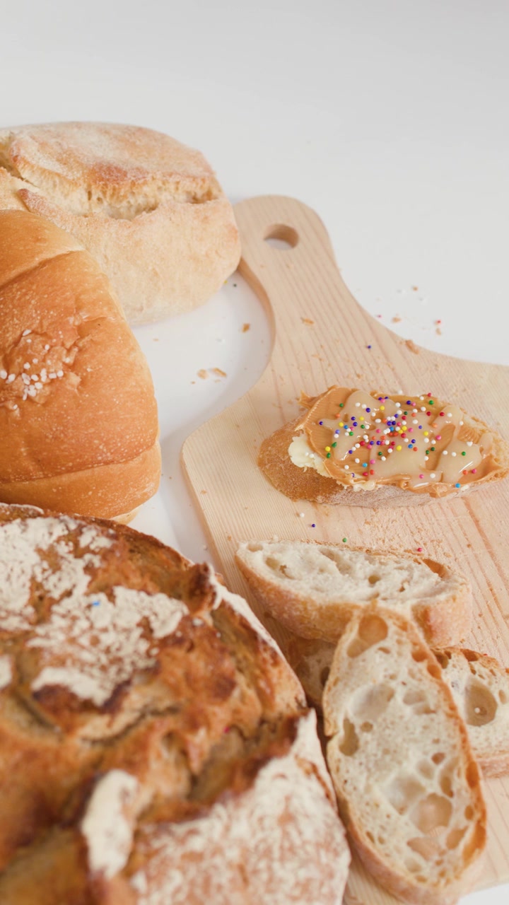 Overhead camera pans across sourdough, baguettes, croissants, and sliced bread on a wooden board.