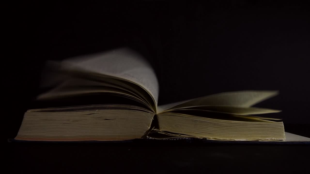 cámara lenta, primer plano de un viejo libro abierto, vintage, con páginas girando en el viento, con destellos brillantes volando alrededor, en una habitación oscura con poca luz, con un entorno negro