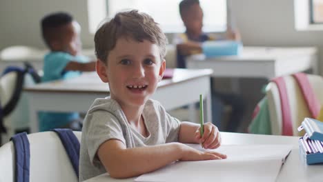 Video-of-happy-caucasian-boy-sitting-at-desk-during-lesson-in-classroom