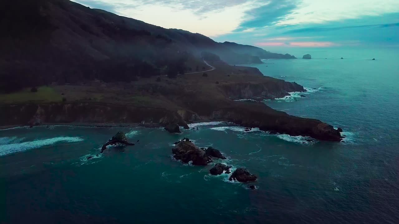 Orbita veloce attorno a un'enorme penisola rocciosa oceanica erosa dalle onde che si infrangono al crepuscolo a Sand Dollar Beach a Big Sur, California