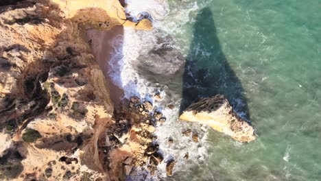 above clifftops as sun casts shadows of large rock formations on golden sand beach