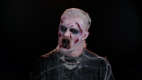 sinister man in costume of halloween crazy zombie with bloody wounded scars face trying to scare