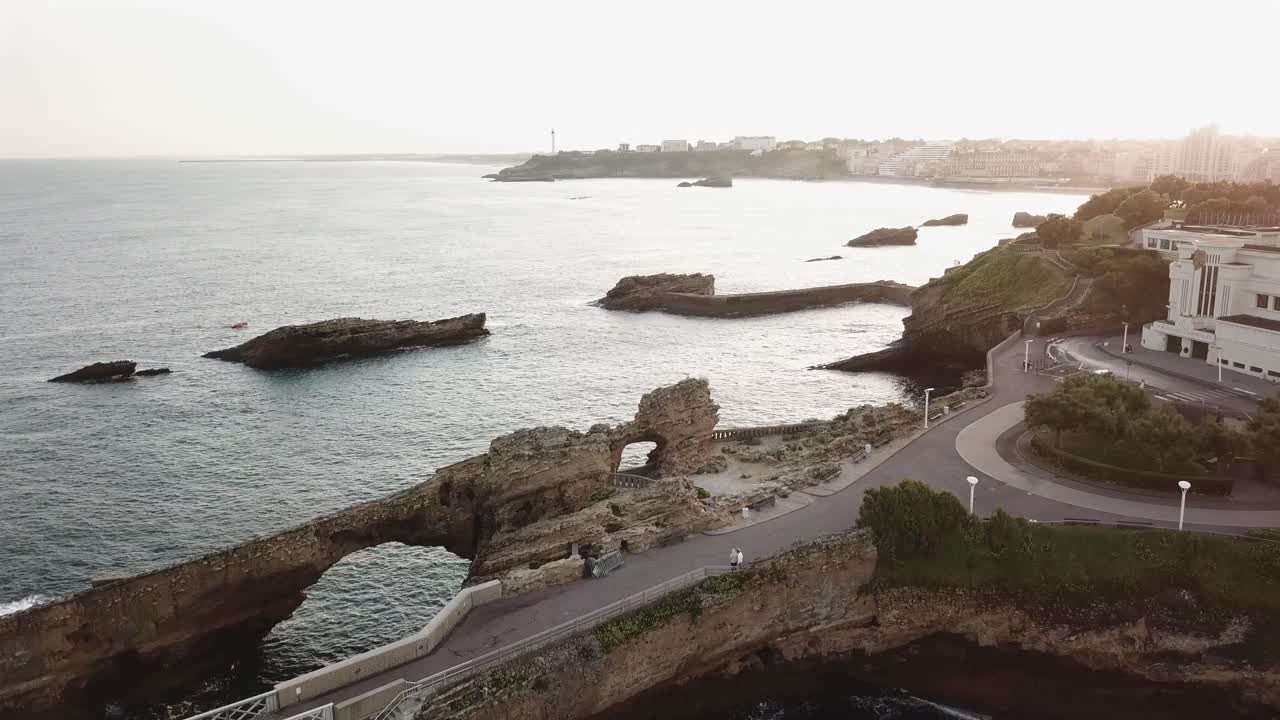 Biarritz coastline, Rocher de la Vierge bridge and Atlantic Ocean during golden hour sunset, French Basque Country, France. Aerial forward
