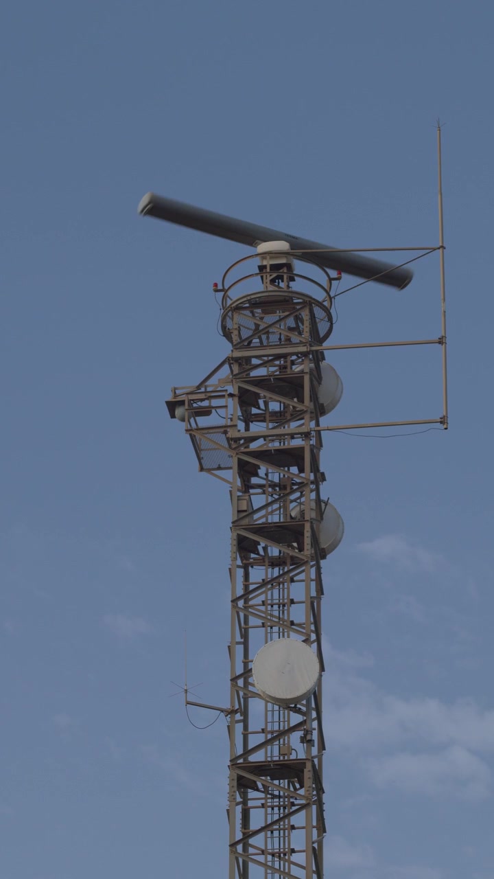 Scatto verticale di un'antenna radar marina che ruota in cima a una torre di comunicazione in acciaio sotto un cielo sereno. Ideale per contenuti marittimi, di navigazione e di telecomunicazioni