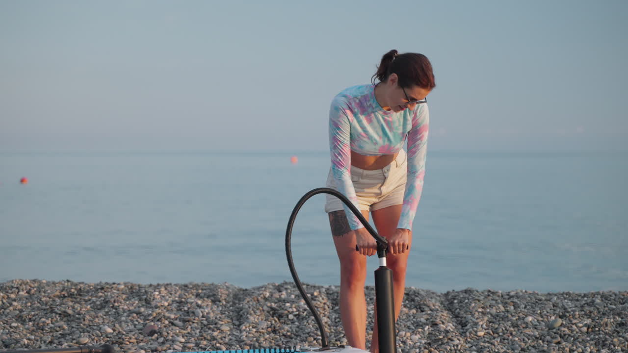 mujer inflando una tabla de paddle de pie en la playa