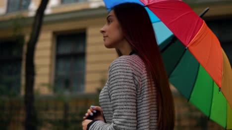 close up view of a young beautiful woman walking and spinning her colorful umbrella in a rainy day in the city streets