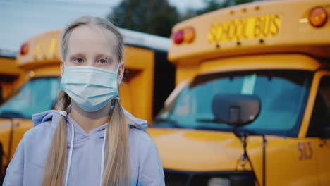 retrato de una escolar en una máscara protectora contra el fondo de una serie de autobuses escolares