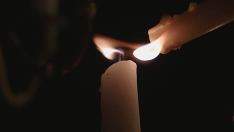 a lone white candle being lite by another candle in slow motion