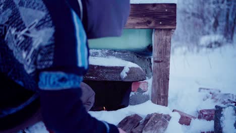 the man is adding small pieces of firewood to heat the diy hot tub - close up