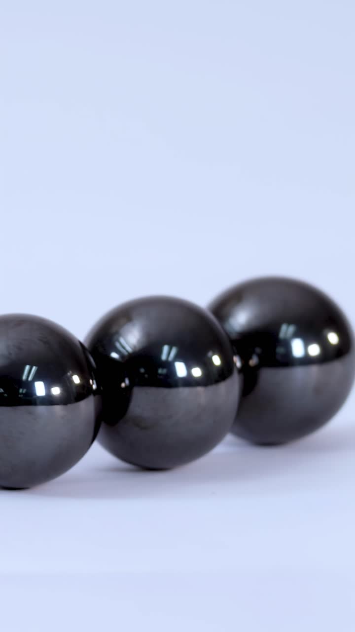 Primo piano di tre sfere magnetiche metalliche che rotolano insieme su uno sfondo bianco pulito.