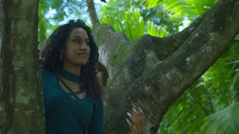 una joven de cabello rizado sonríe mientras se sienta en un gran tronco de árbol