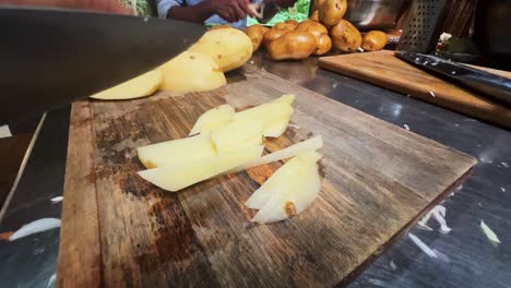 manos con un cuchillo cortando las patatas en la tabla de madera en la cocina