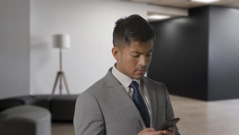 serious businessman in suit messaging on mobile phone in modern open plan office