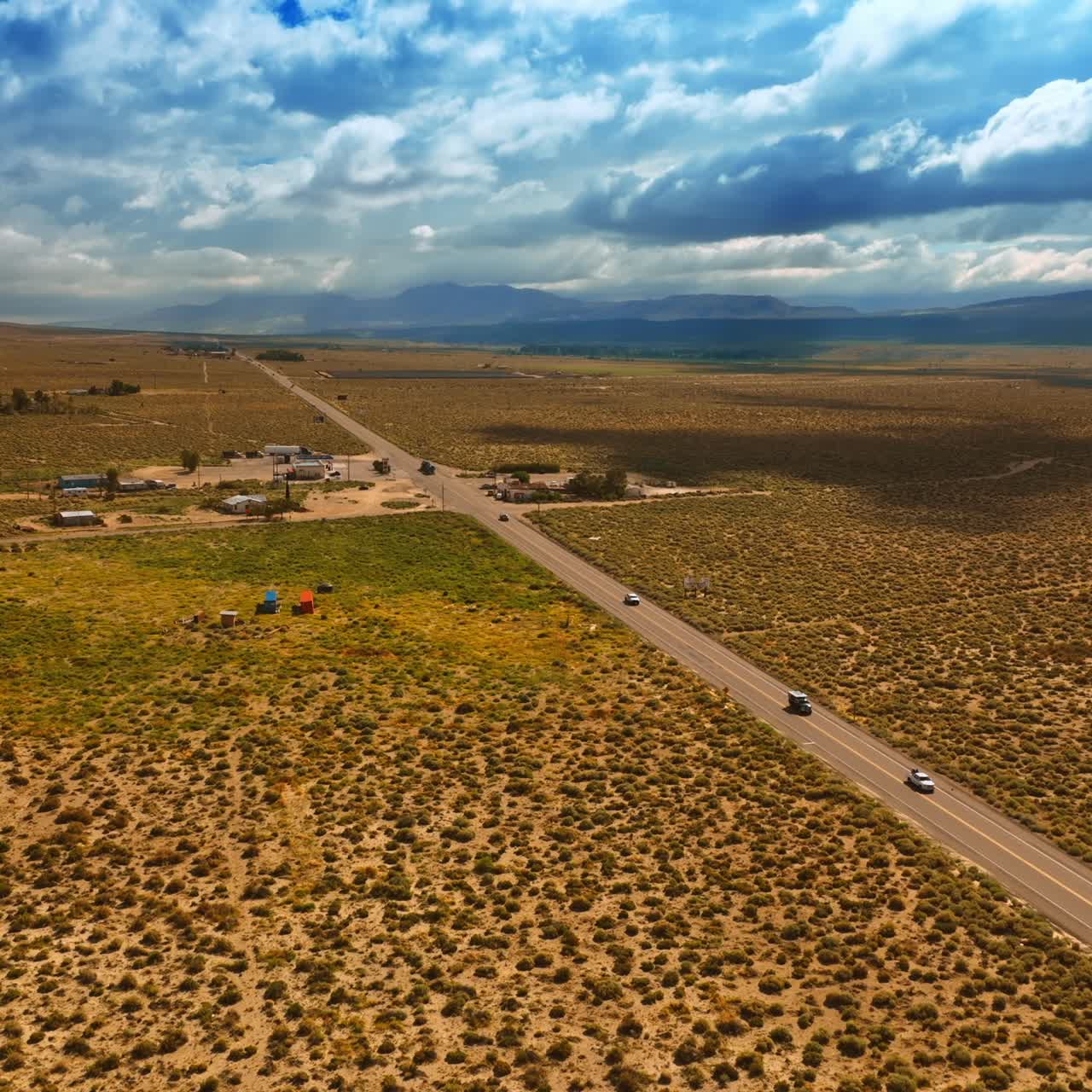 A few houses near the highway in Nevada desert. Rainy cloudscape covering the sky above the landscape. Aerial view