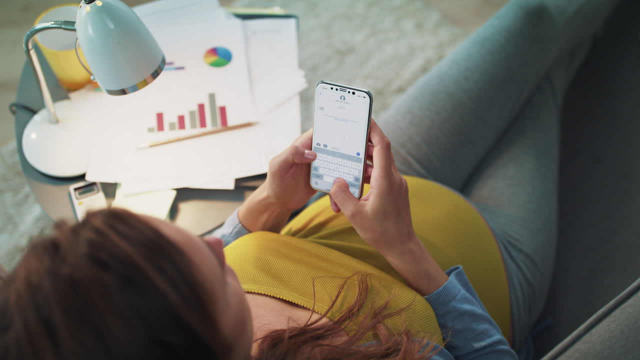 una mujer de negocios embarazada enviando mensajes de texto en su teléfono inteligente en casa a cámara lenta.
