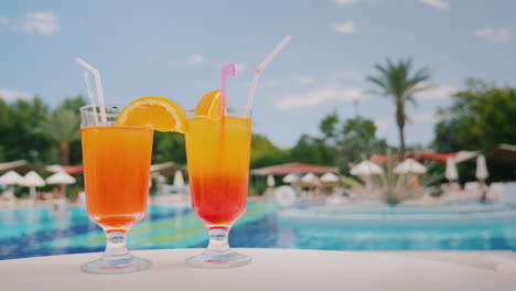 two cool cocktails stand on the table on the background of the pool and palm trees paradise and luxu