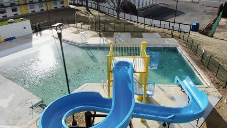 Blue-water-slide-at-hotel-motel-in-disrepair,-dirty-pool-water,-aerial-drone-view,-one-star-review,-awful-trip,-request-money-back-,-disappointment,-terrible-experience