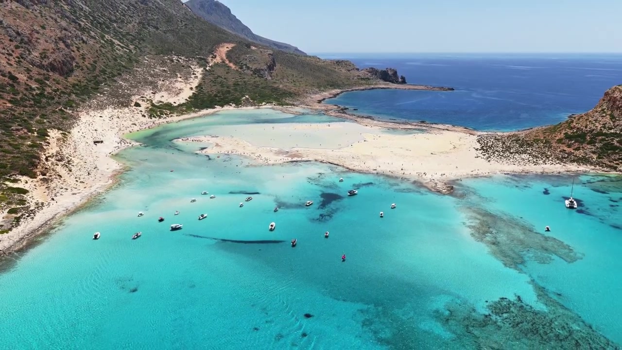 Dronekuva Balosin laguunista veneineen matalassa turkoosissa vedessä valkohiekkaisen tombolon vieressä, Balos, Kreikka