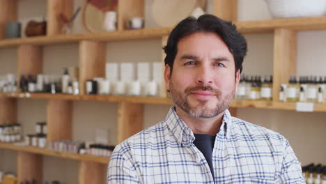 portrait of male owner of gift store standing in front of shelves with cosmetics and candles