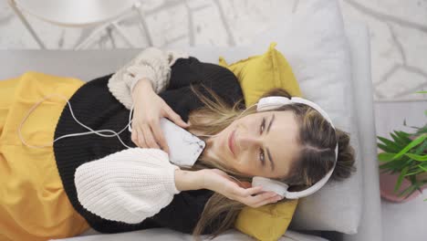 young woman is resting on comfortable sofa, listening to music with eyes closed.