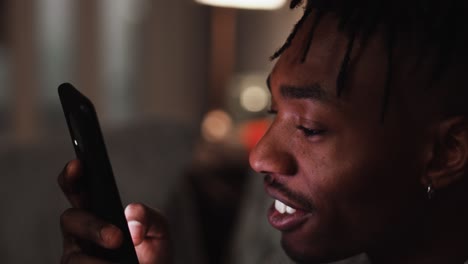 a young black male brings phone closer to his face while scrolling and smiling at his smart phone