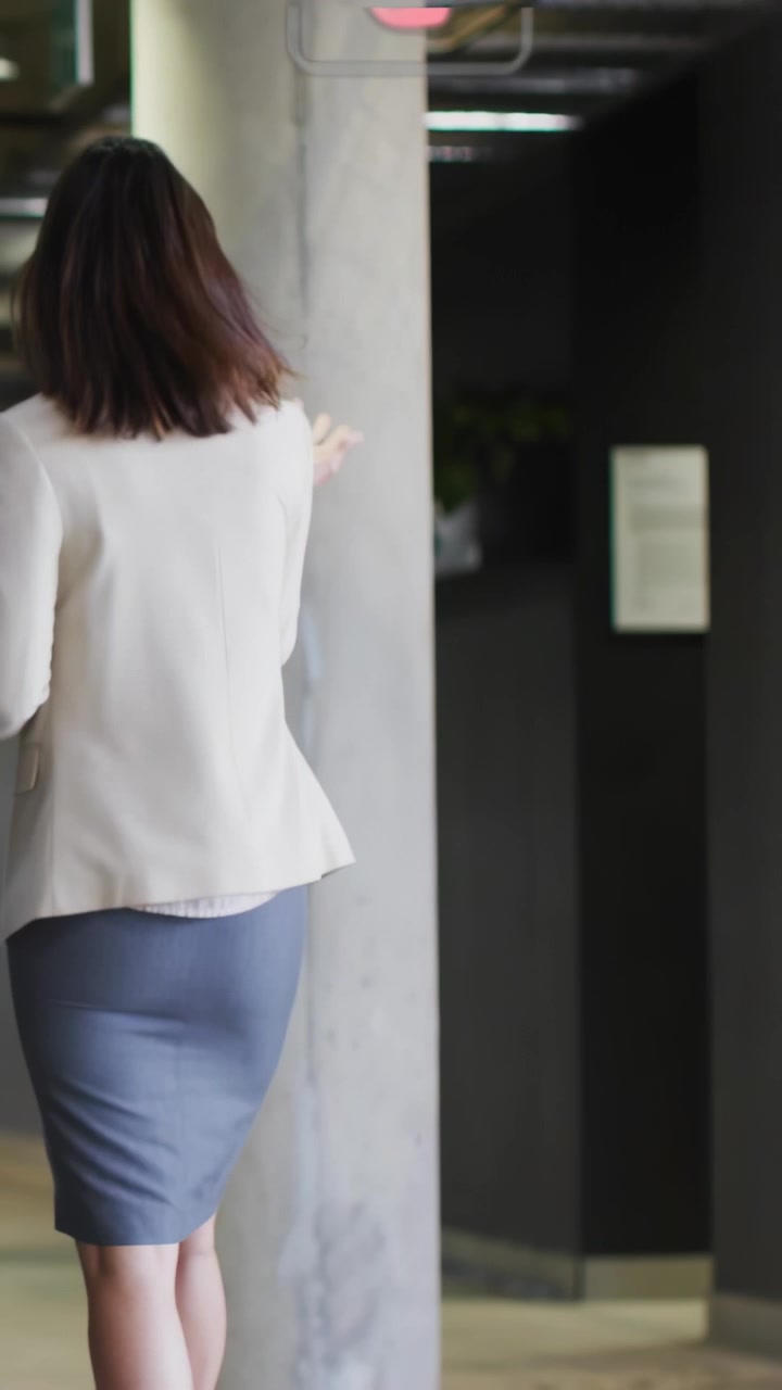 Video vertical: Mujer caminando por el pasillo de la oficina con una tableta, respondiendo a un compañero mientras iconos HUD se superponen.