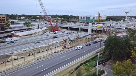 slow upward rising aerial drone shot of busy highway exit showing bridge overpass intersection with vehicular traffic, road construction zone, road construction equipment, and crane