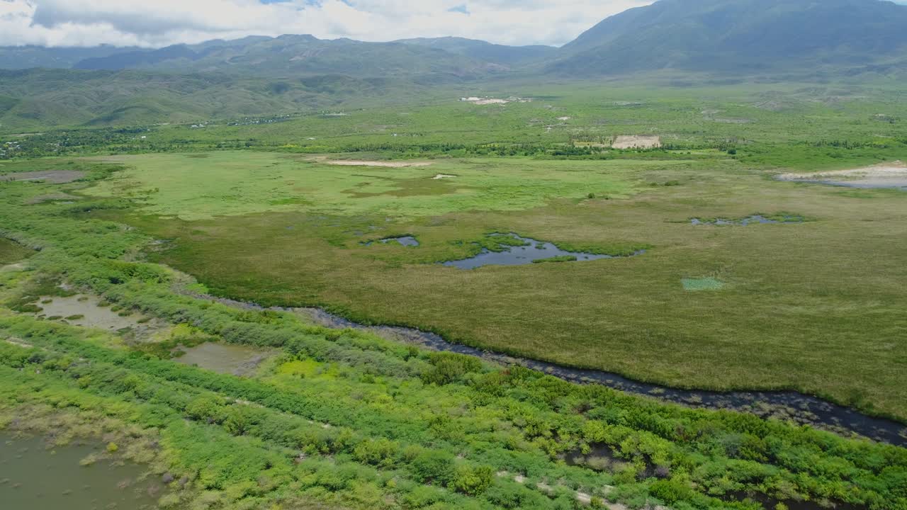 Pequenos cursos d'água e lagos situados em terras agrícolas gramadas com montanhas verdes épicas ao fundo