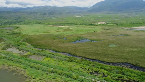 Small-Water-Streams-and-lakes-sit-in-grassy-farmland-with-epic-green-mountains-in-the-background