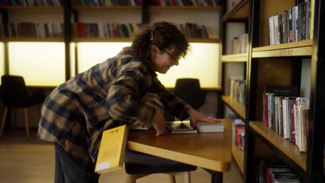 una chica con el cabello rizado un estudiante lleva una pesada pila de libros que se desmorona en sus manos en la biblioteca