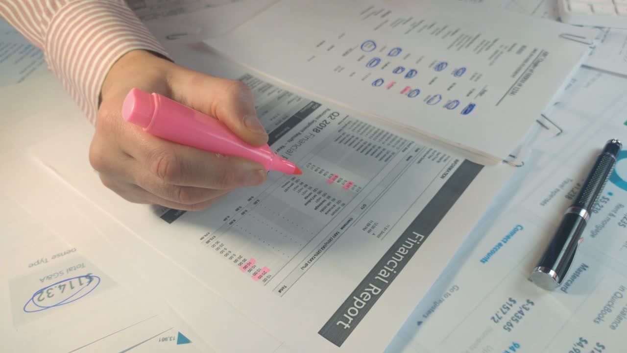 primer plano de manos subrayando números con un marcador en un informe financiero