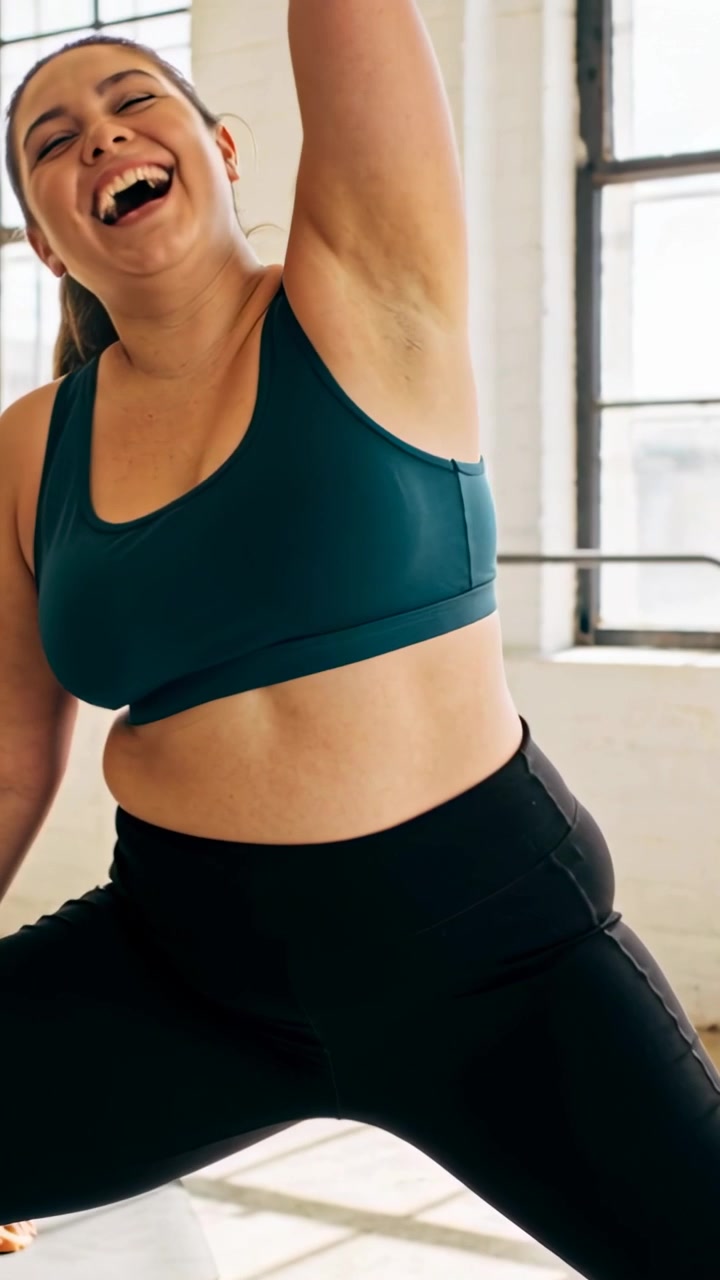 Video verticale: La telecamera si avvicina, donna in reggiseno e leggings color verde acqua che fa squat per il fitness vicino alle finestre dello studio.