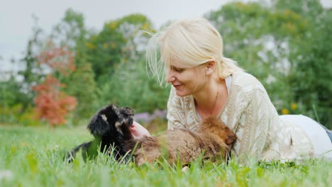 happy with your favorite puppies. a woman is playing with two dogs, lying on a lawn in her yard
