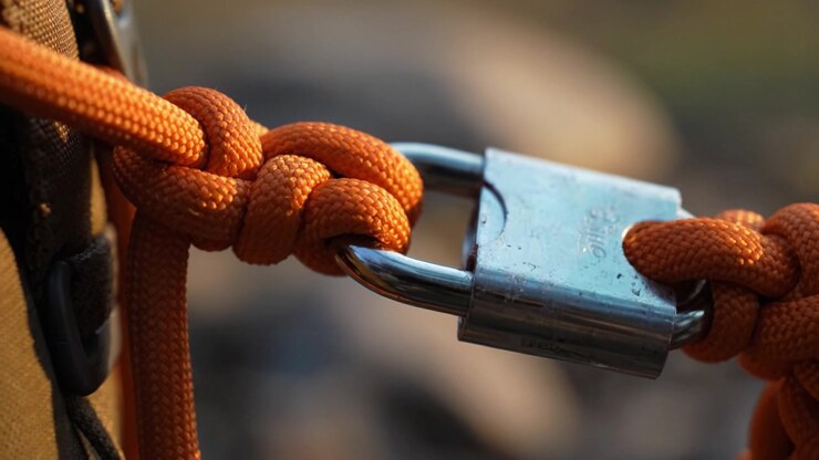 A close-up view of a secured padlock attached to a vibrant orange rope, showcasing intricate knotting techniques and details of the clasp mechanism in natural light.