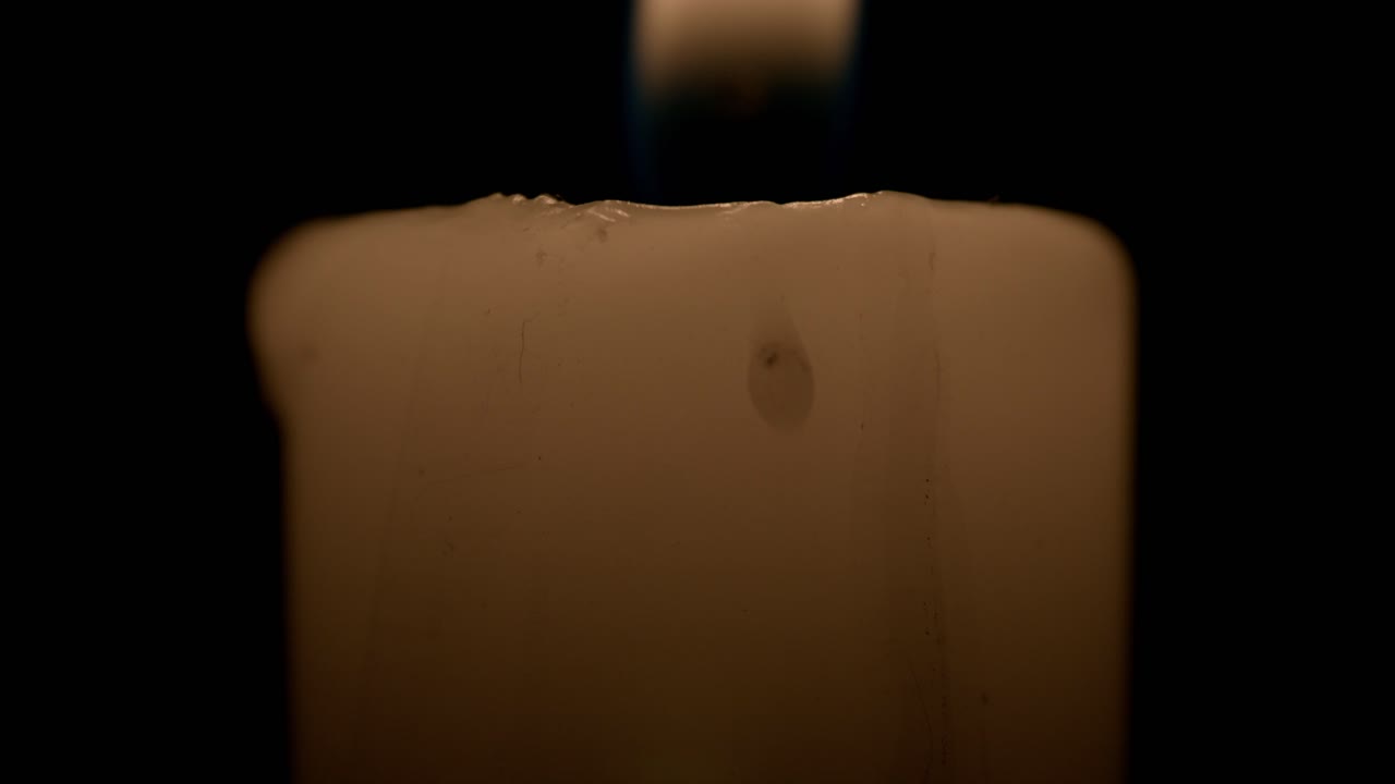 A calming close-up shot of a flickering candle flame illuminating the darkness. The warm glow casts soft, ambient light, creating a tranquil atmosphere ideal for relaxation
