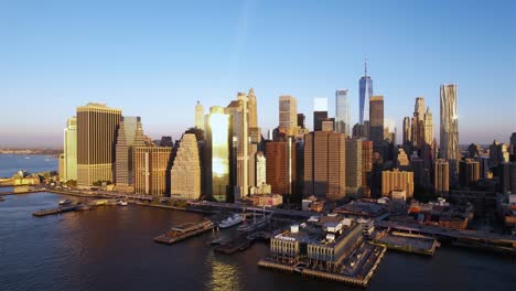 ascending aerial view in front of the golden hour lit skyline of lower manhattan, nyc