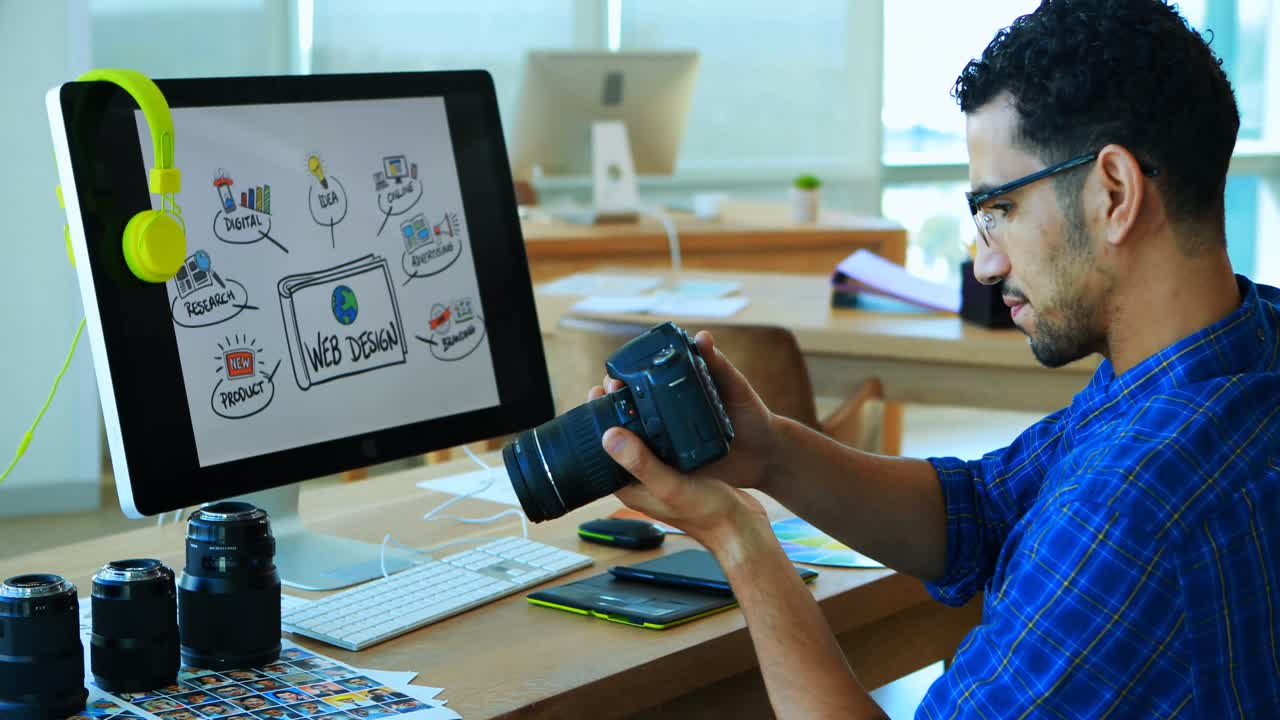 Male graphic designer looking at photos in digital camera at his desk