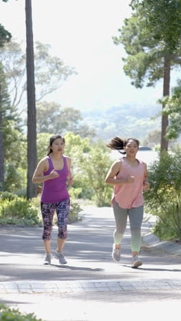 felices amigas asiáticas corriendo cerca del bosque en un día soleado, en cámara lenta
