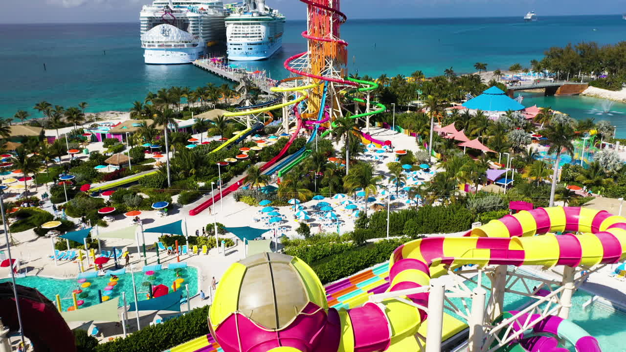 Cinematic arial shot of CoCoCay island with water slides and a Royal Caribbean cruise ship in the background, quickly tilting upward