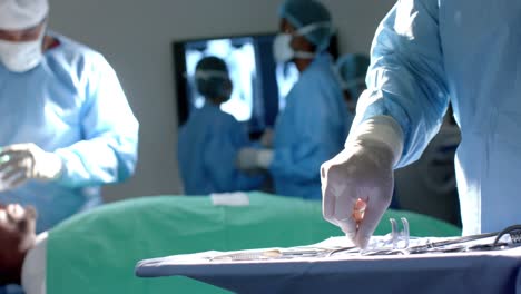 midsection of biracial male surgeon preparing surgical instruments in operating theatre, slow motion