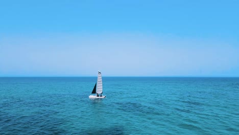 An-aerial-view-of-Two-Catamaran-sailboats-are-floating-on-the-water,-each-with-a-person-controlling-it-close-together,-and-there-is-another-boat-further-away-in-the-background