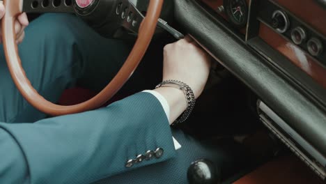 man in suit turns ignition key in vintage car interior with wooden steering and chrome details